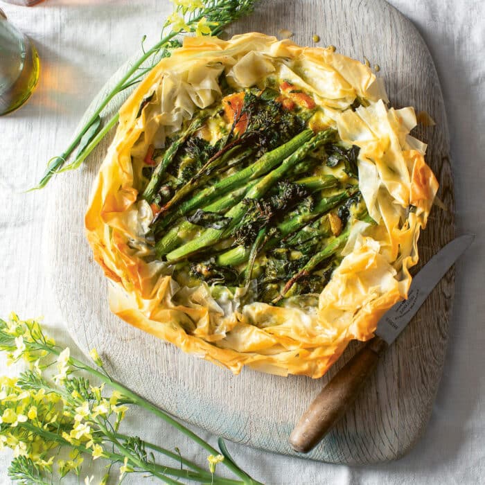 A filo pastry tart with asparagus and other green vegetables, on a wooden board on a table