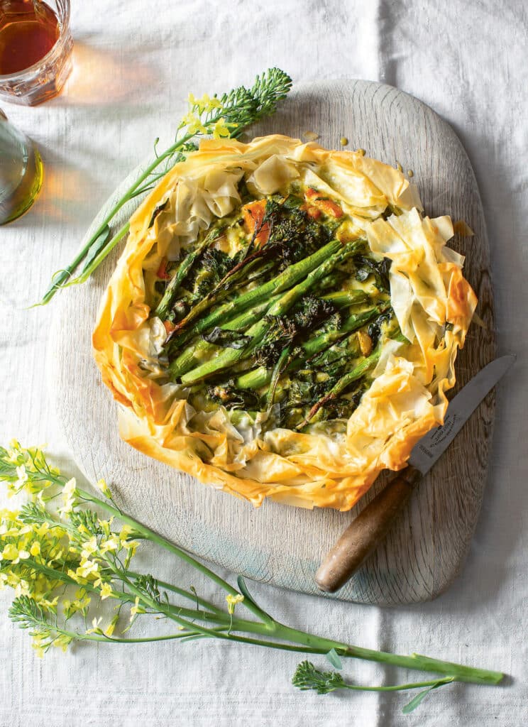 A filo pastry tart with asparagus and other green vegetables, on a wooden board on a table