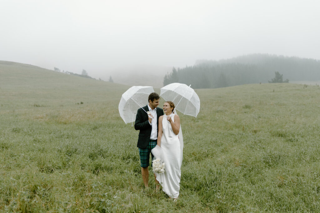 A bride and groom standing in a grassy field with umbrellas