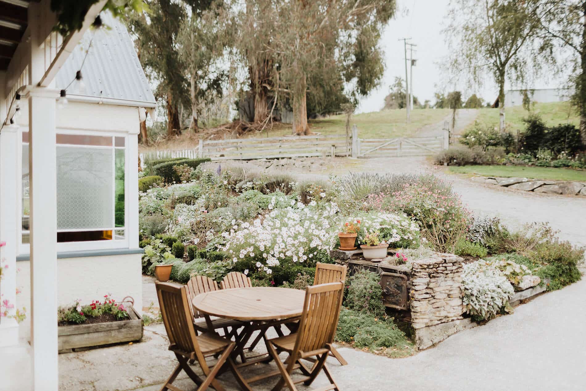 Wooden round outdoor table and chairs, vibrant garden behind