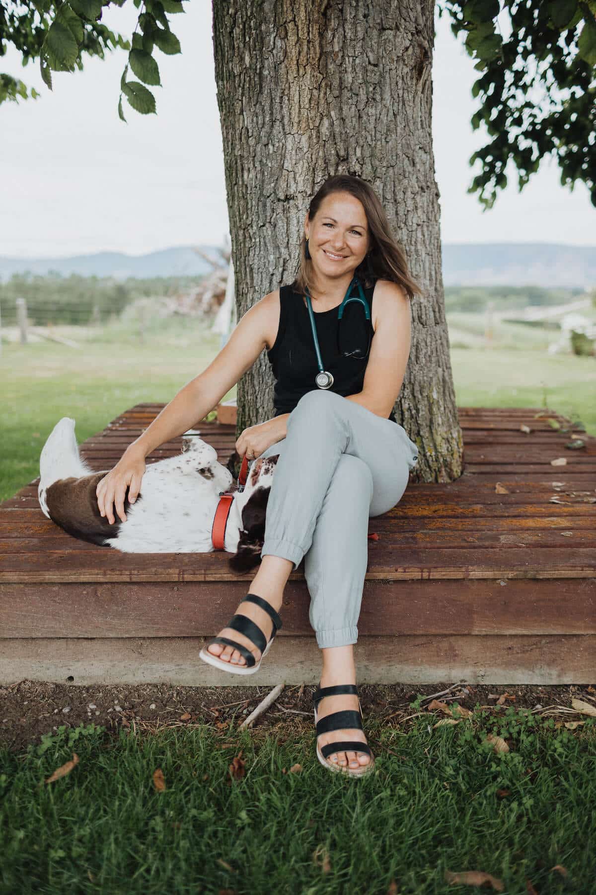 Woman sits in front of a tree with a dog