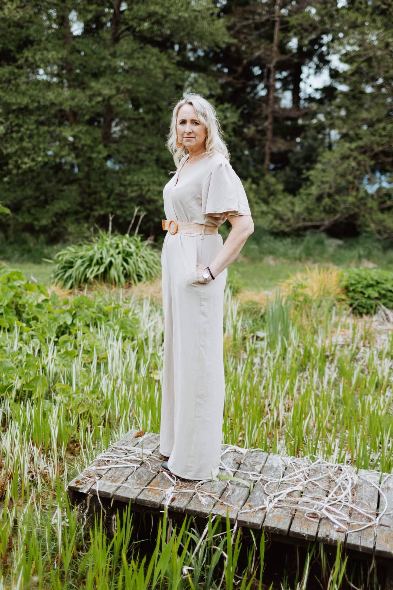 Woman stands on a wooden boardwalk in a green rural property.