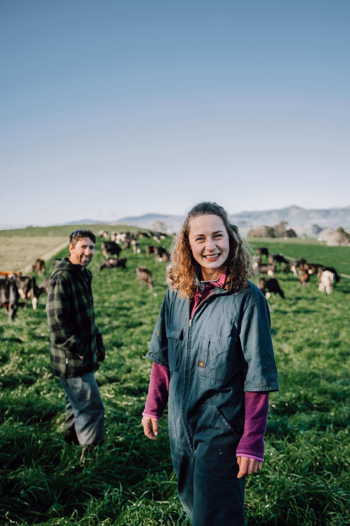 Woman and man smiling at the camera from a paddock with cows