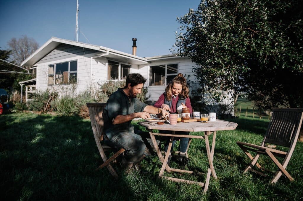 Man and woman sit at table outside their house on the farm eating pancakes.