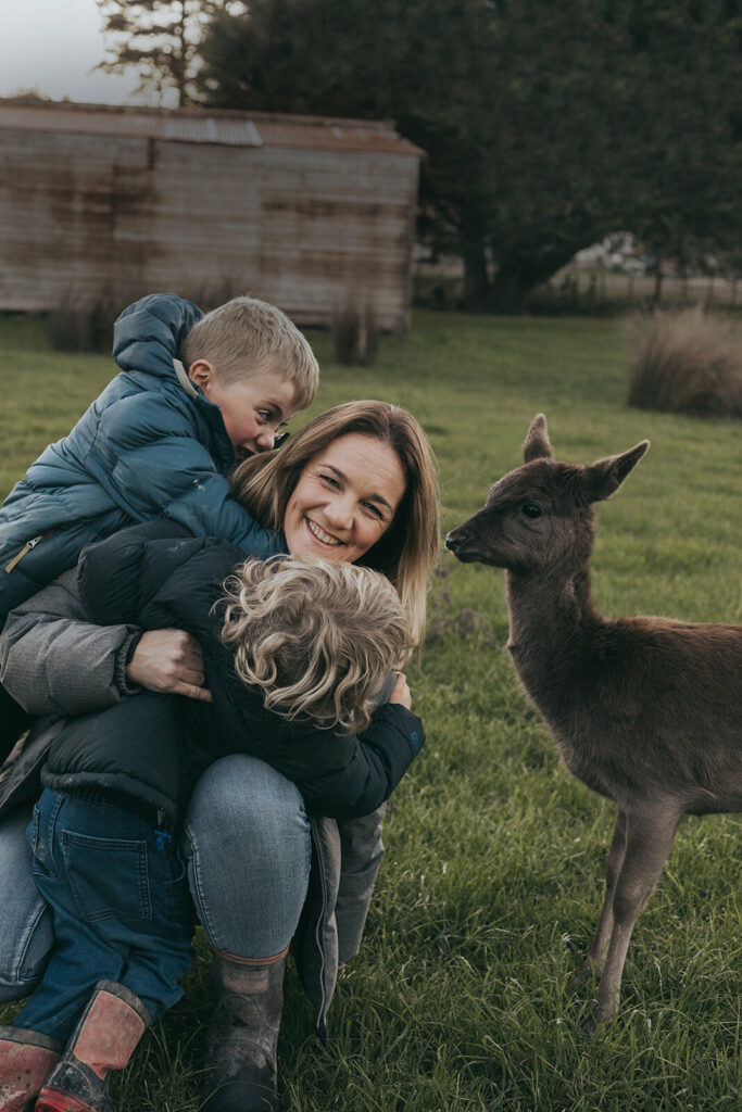 A women and two young boys hug next to a deer