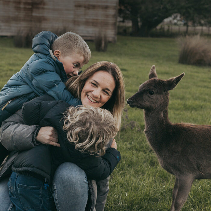 A women and two young boys hug next to a deer