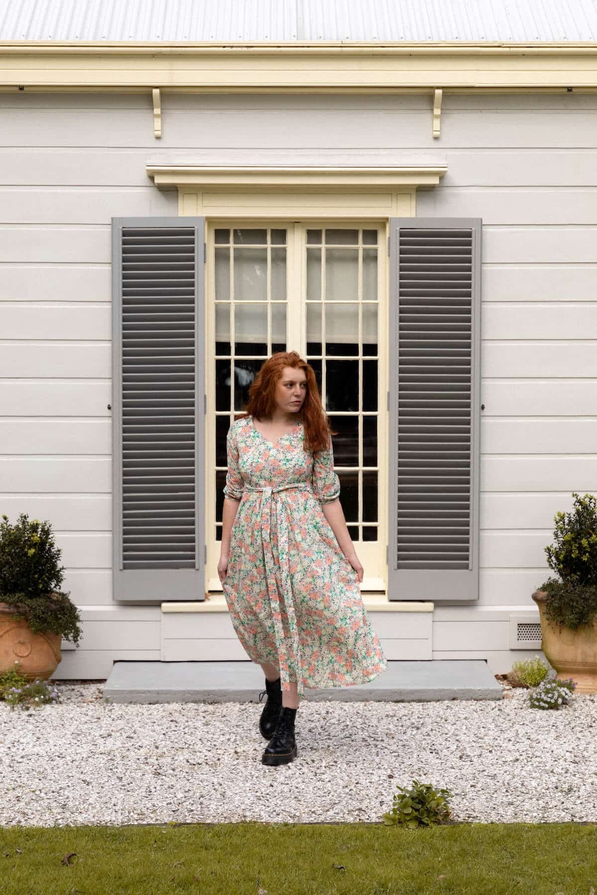 Woman models floral dress in front of weatherboard heritage house with timber shutters