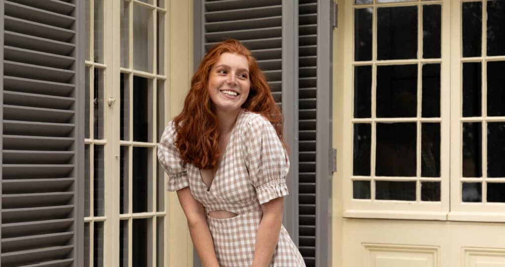 Woman models a checkered dress in front of a heritage house