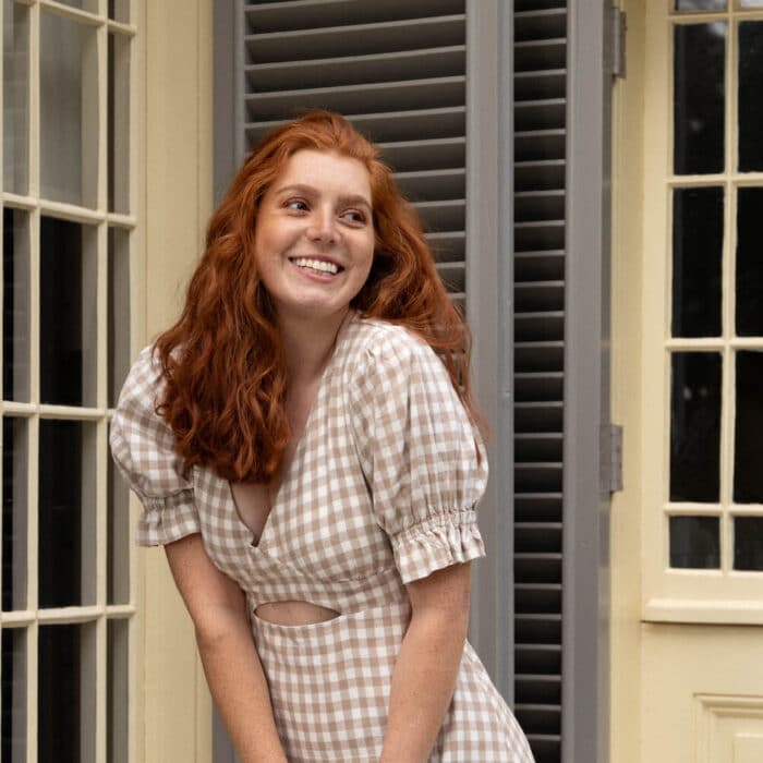Woman models a checkered dress in front of a heritage house
