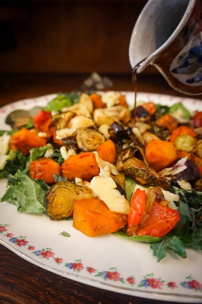 Close-up image of dressing being poured onto a roast vegetable salad.