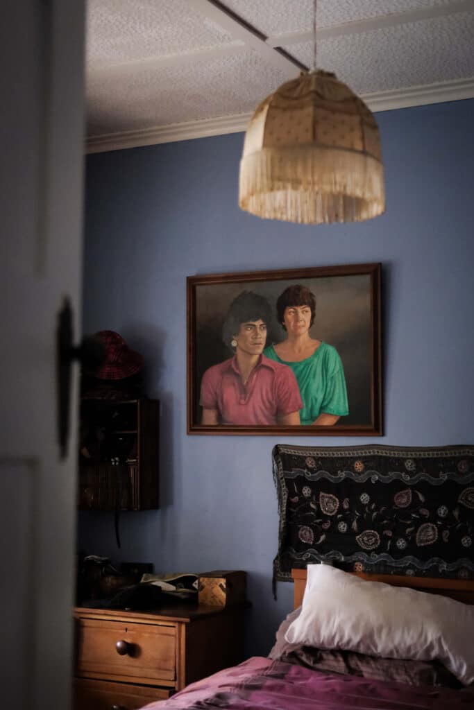 Photo of a painting of a couple, hung on a blue wall over a bed