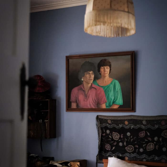 Photo of a painting of a couple, hung on a blue wall over a bed