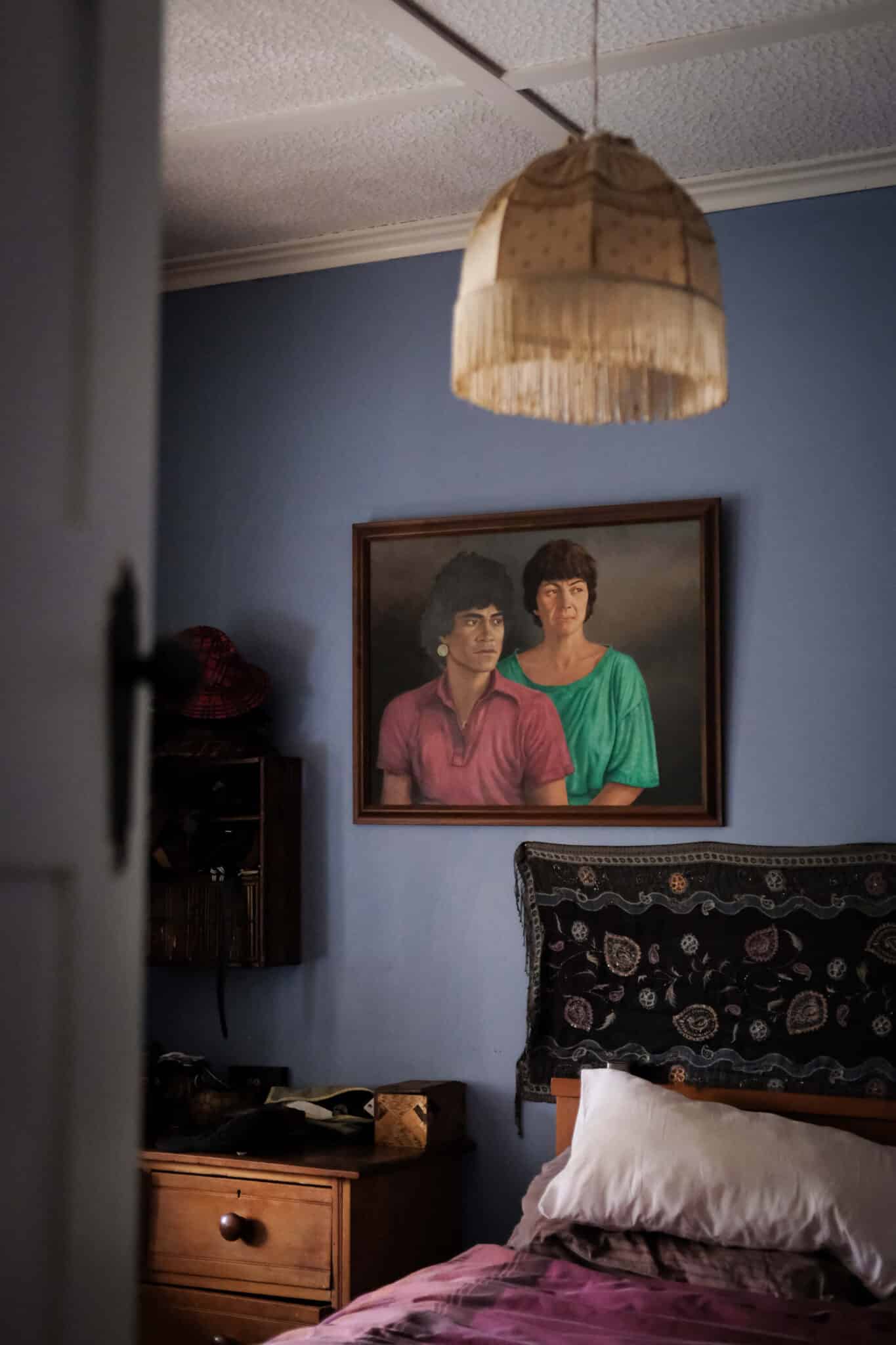 Photo of a painting of a couple, hung on a blue wall over a bed