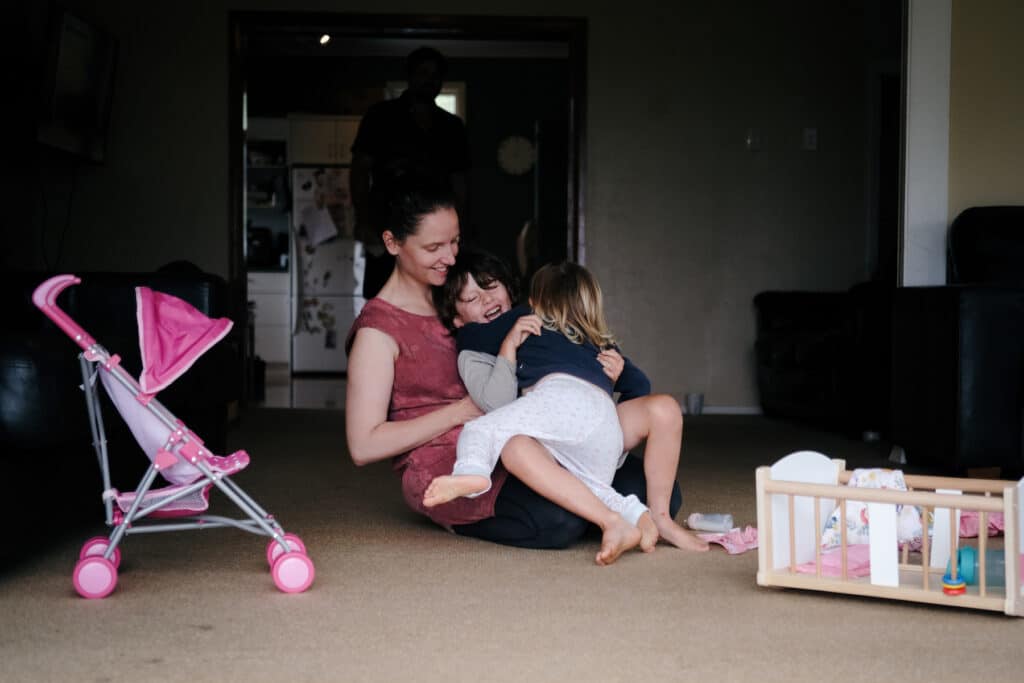 Woman plays with her two young children on the floor at their home