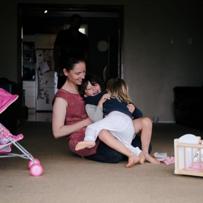 Woman plays with her two young children on the floor at their home