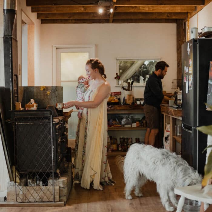 Woman holding her newborn baby stands in the kitchen of her yurt while her husband does something in the background.