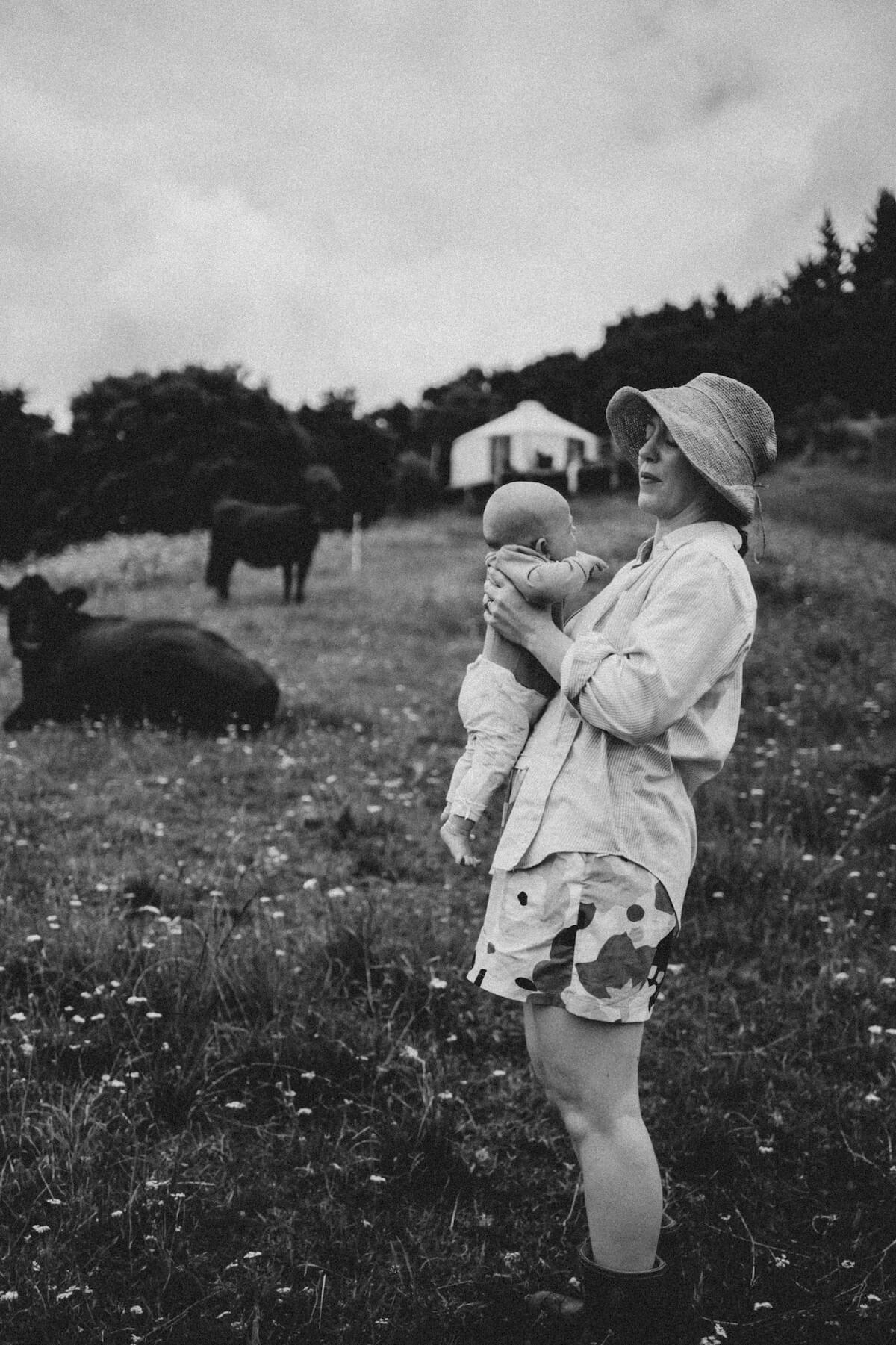 Black and white image of Eloise in a field with cows, holding baby Rosamund.