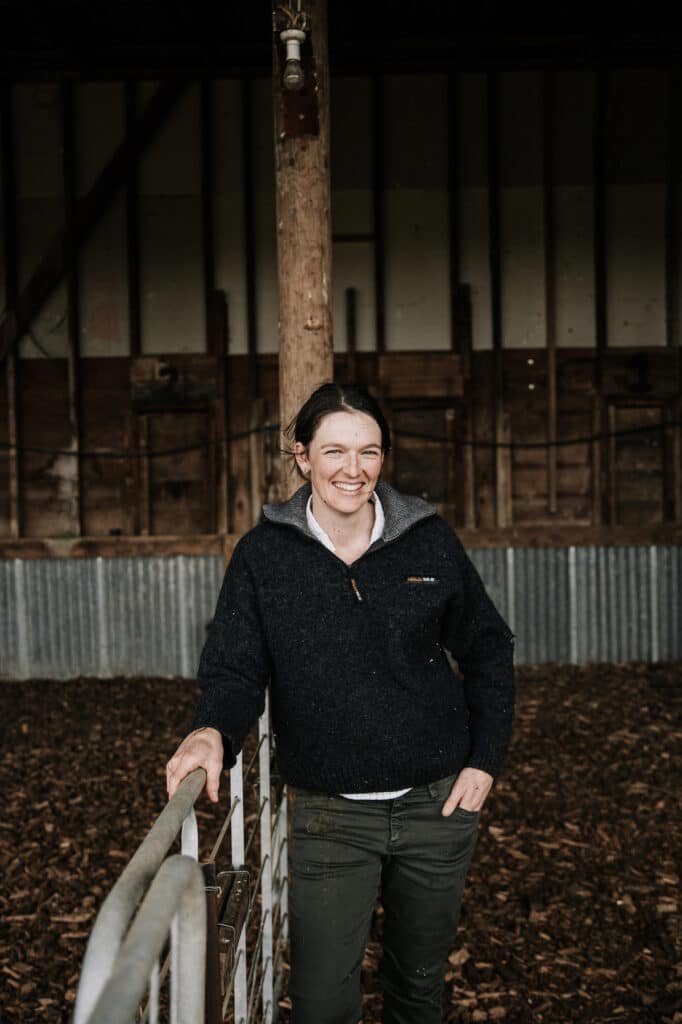 Woman leans against a fence inside a barn.