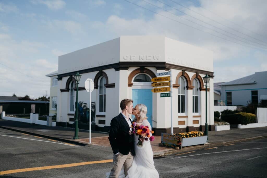 Newlywed couple kiss outside an art deco building in Aparima Riverton