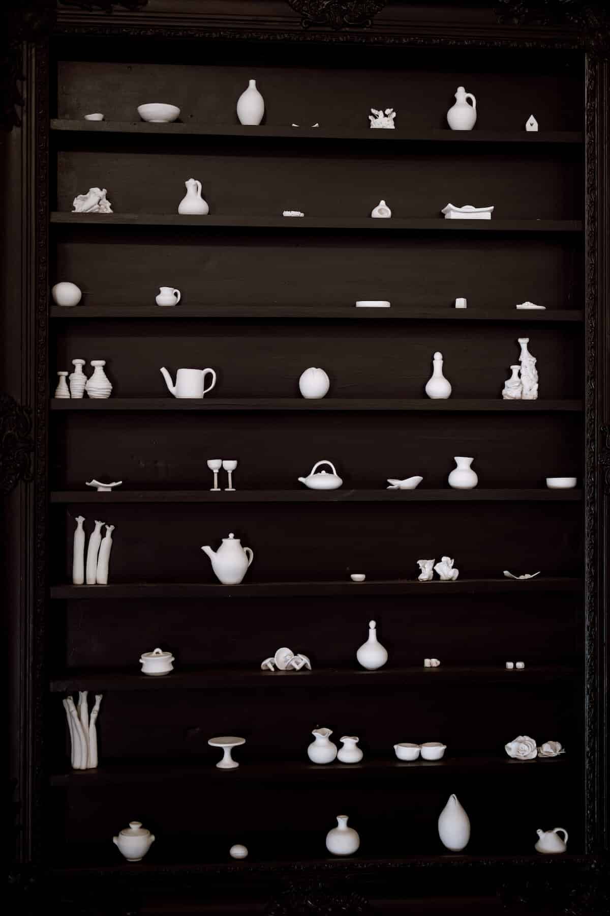 Miniature white ceramic works on black shelving