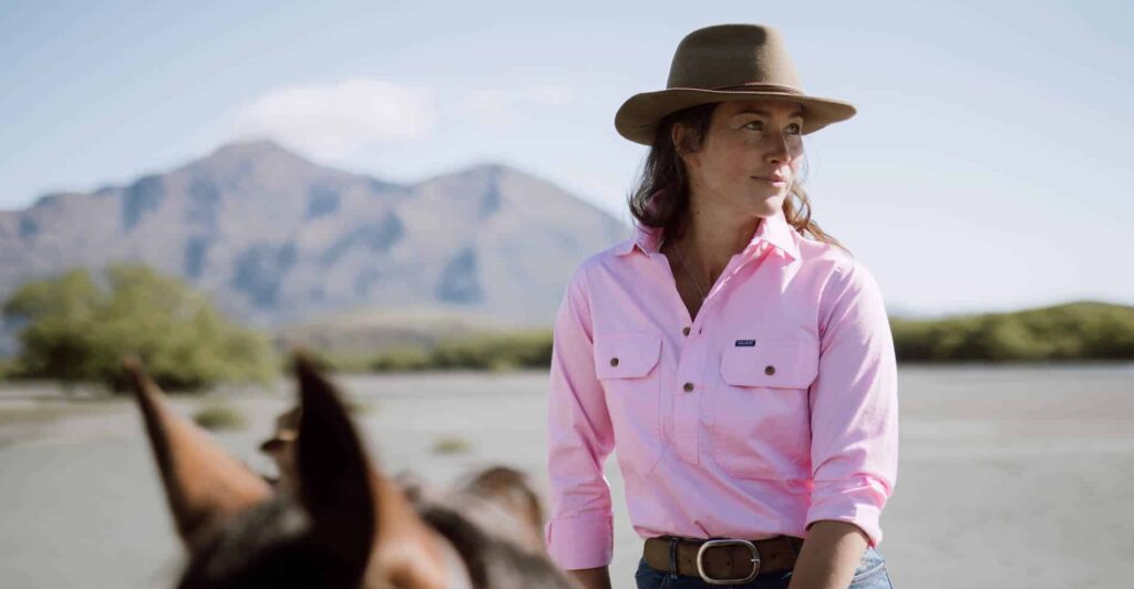 Woman in a pink shirt sits astride a horse in the high-country.