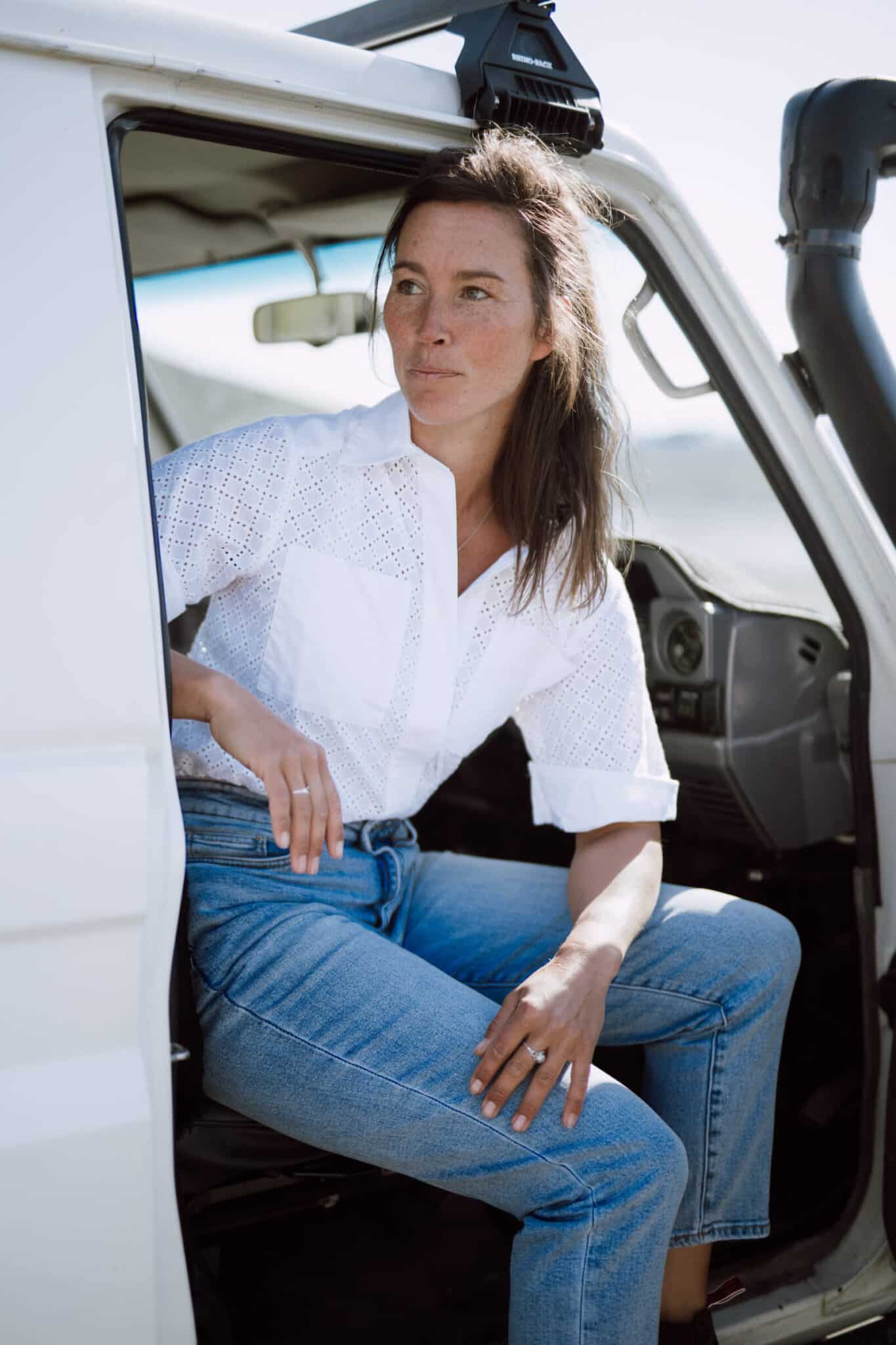 A woman leans out of the passenger seat of a car with the door open.