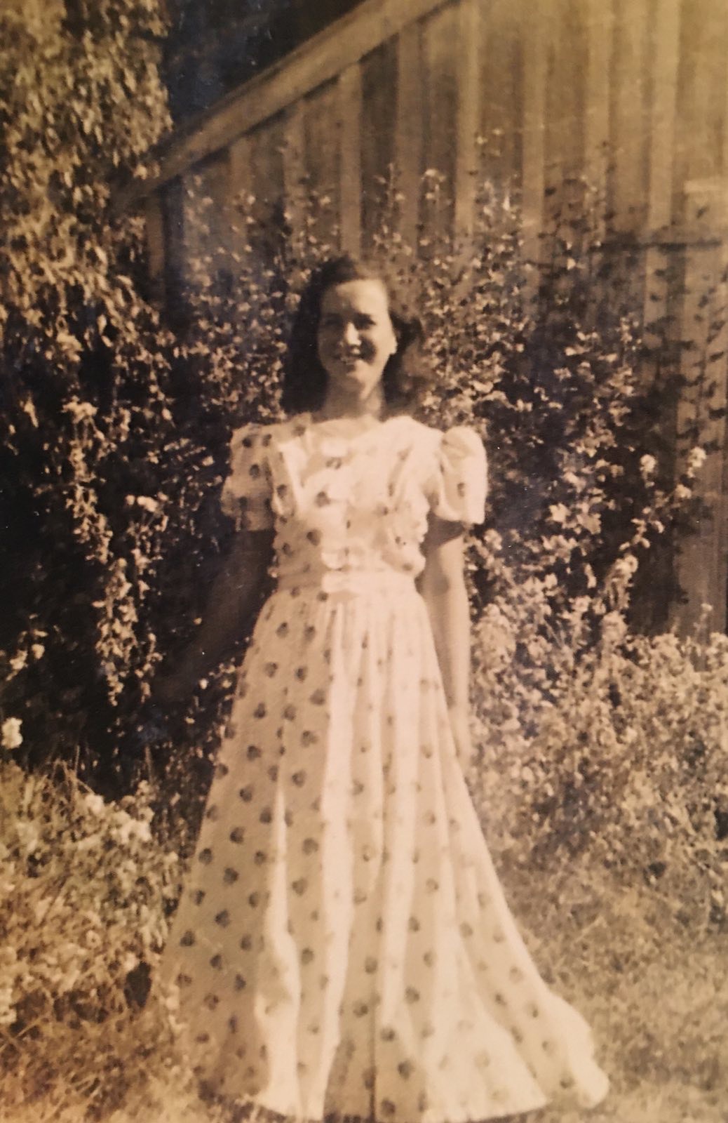 Sepia image of woman in front of a shrub.