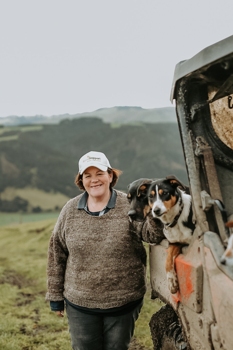 Woman stands beside a muddy farm buggy with two dogs