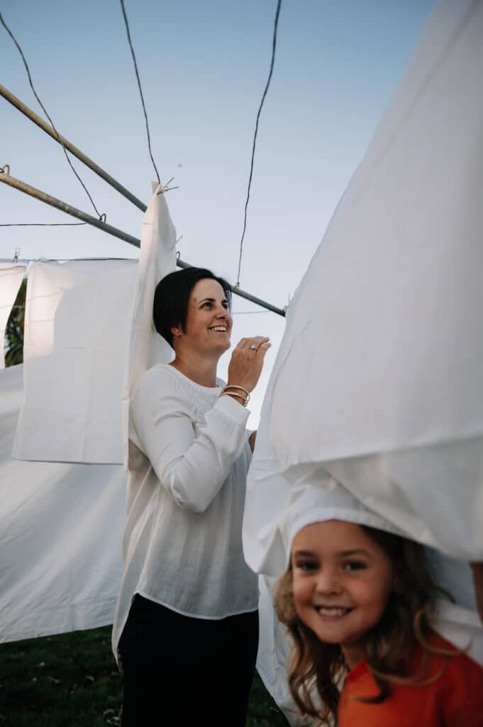 Woman hanging out washing with one of her children playing in a sheet