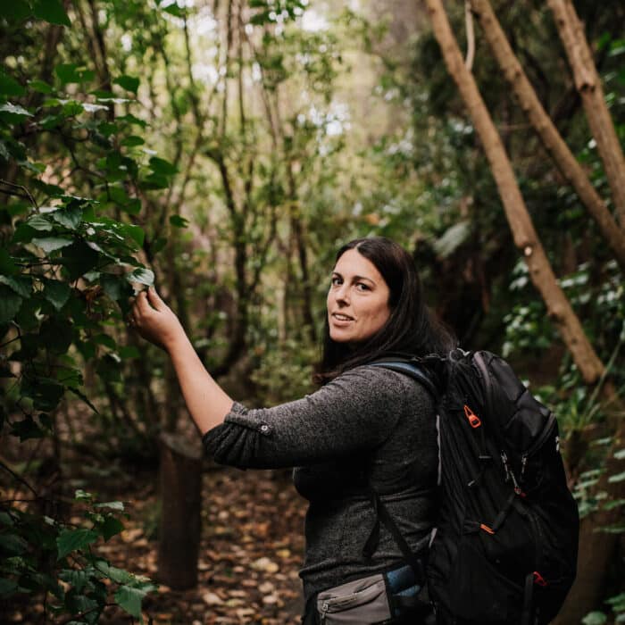 A woman inspects a leaf on a bush walk.
