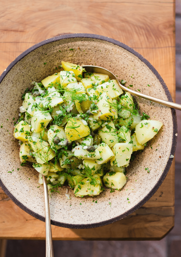 Potatoes and herbs in a salad bowl with serving spoons.
