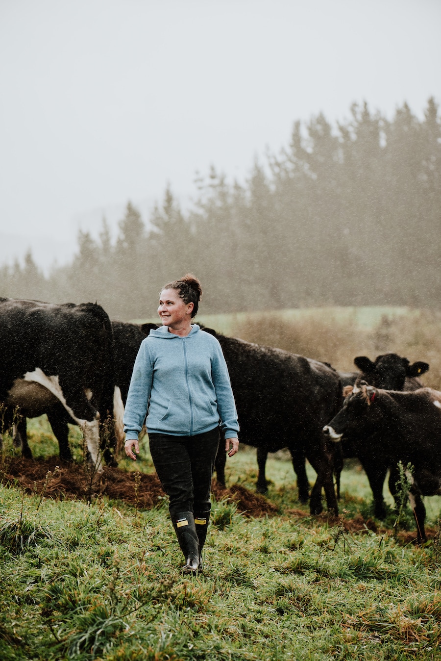 Woman stands in the rain in a paddock of black cows.