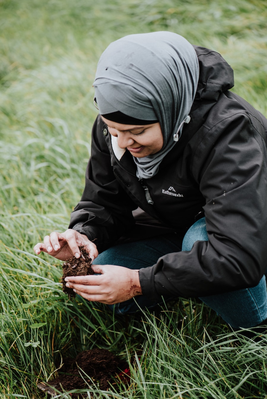 Woman crouches in a paddock to inspect the soil with her hands.