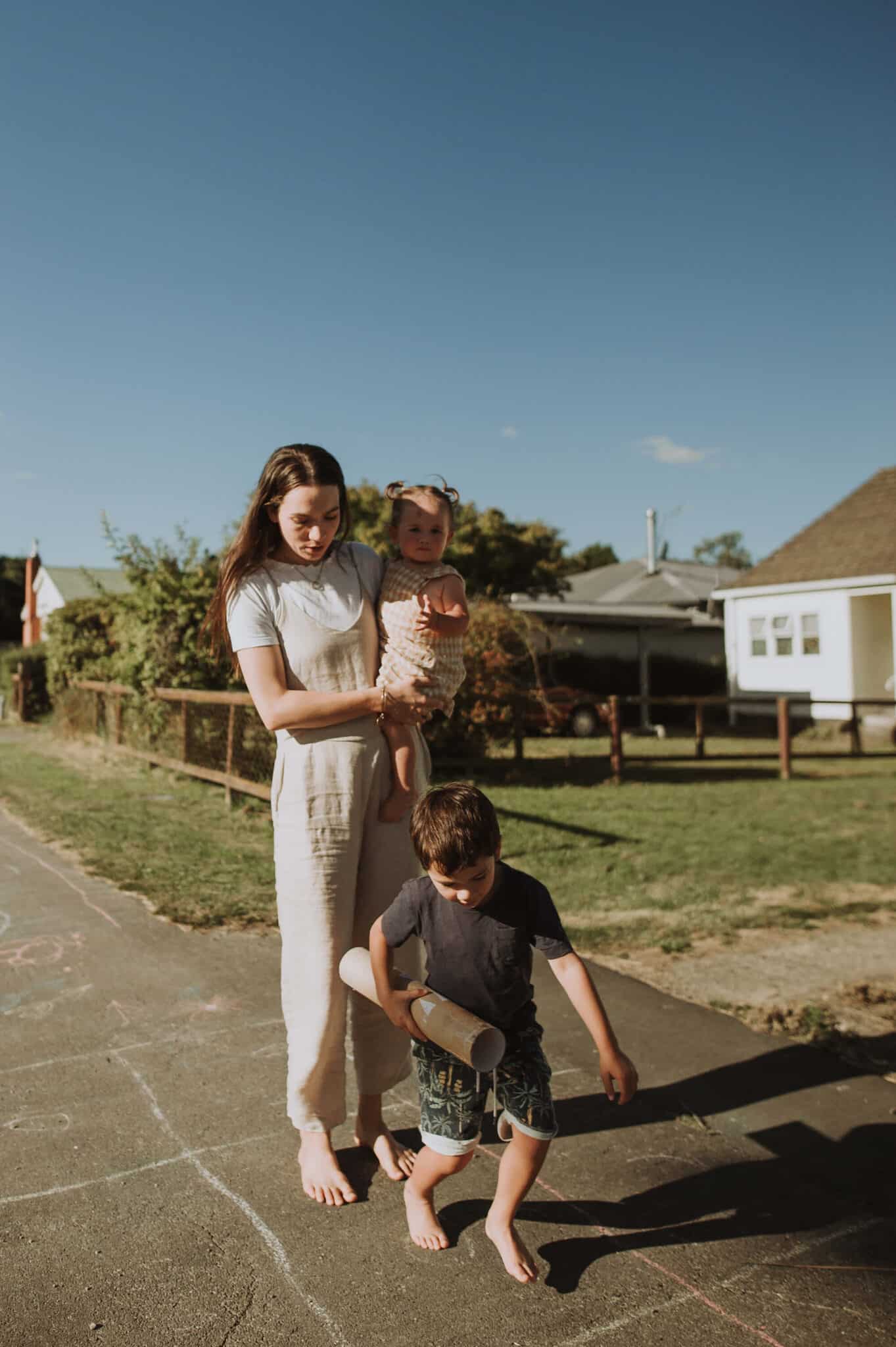Woman and her two young children barefoot on the footpath, playing hopscotch
