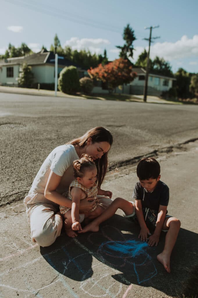 Renee plays with her two young children on the footpath.