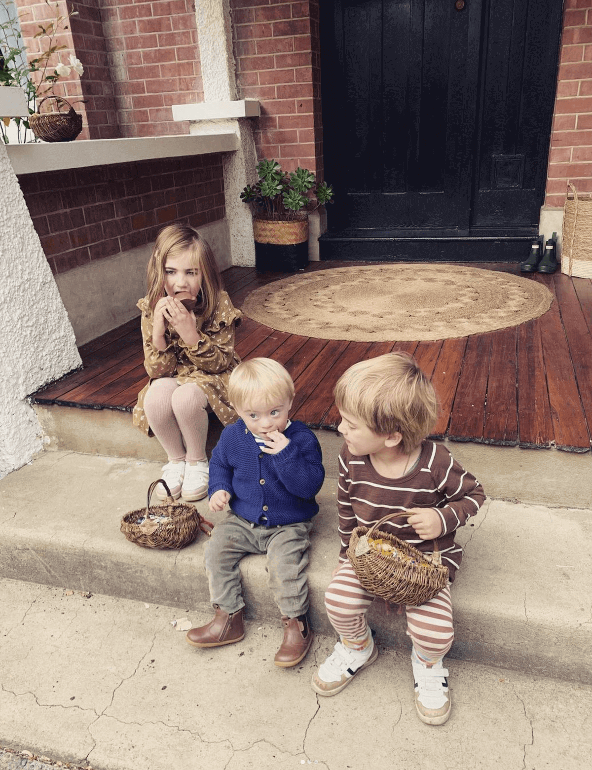 Three young kids sitting out on a front porch with baskets of Easter chocolate.