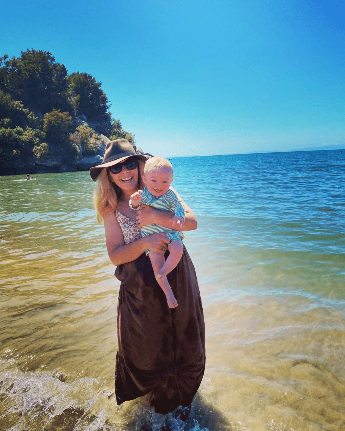 Woman stands in the ocean holding her young Down syndrome son.