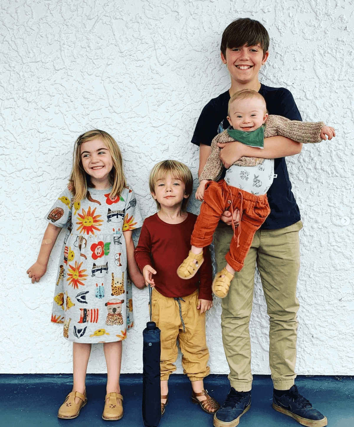 Four siblings stand against a wall.
