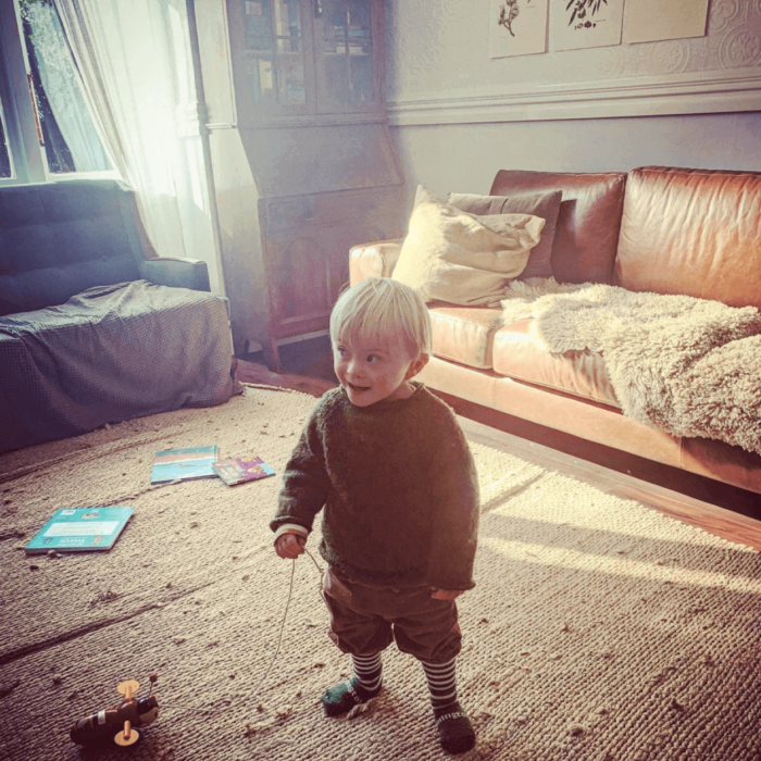 Young Down syndrome boy stands in lounge holding wooden bee toy.