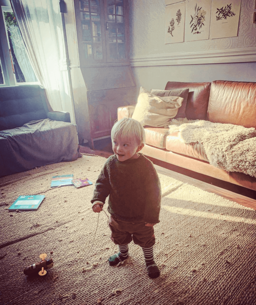 Young Down syndrome boy stands in lounge holding wooden bee toy.