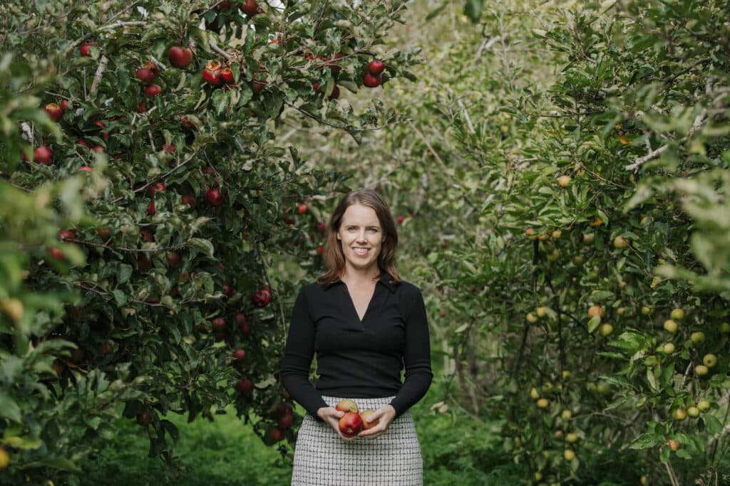 Dr Shannon Davis stands in an apple orchard, holding apples