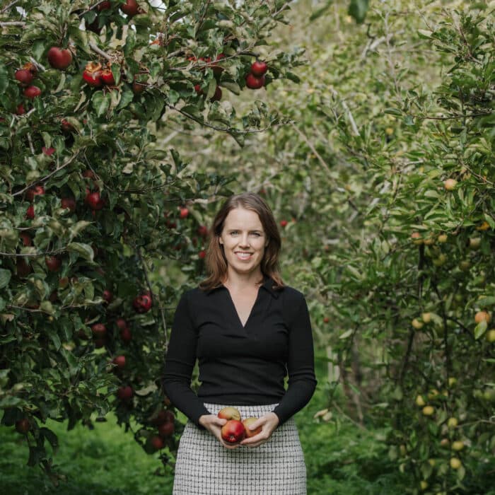 Dr Shannon Davis stands in an apple orchard, holding apples