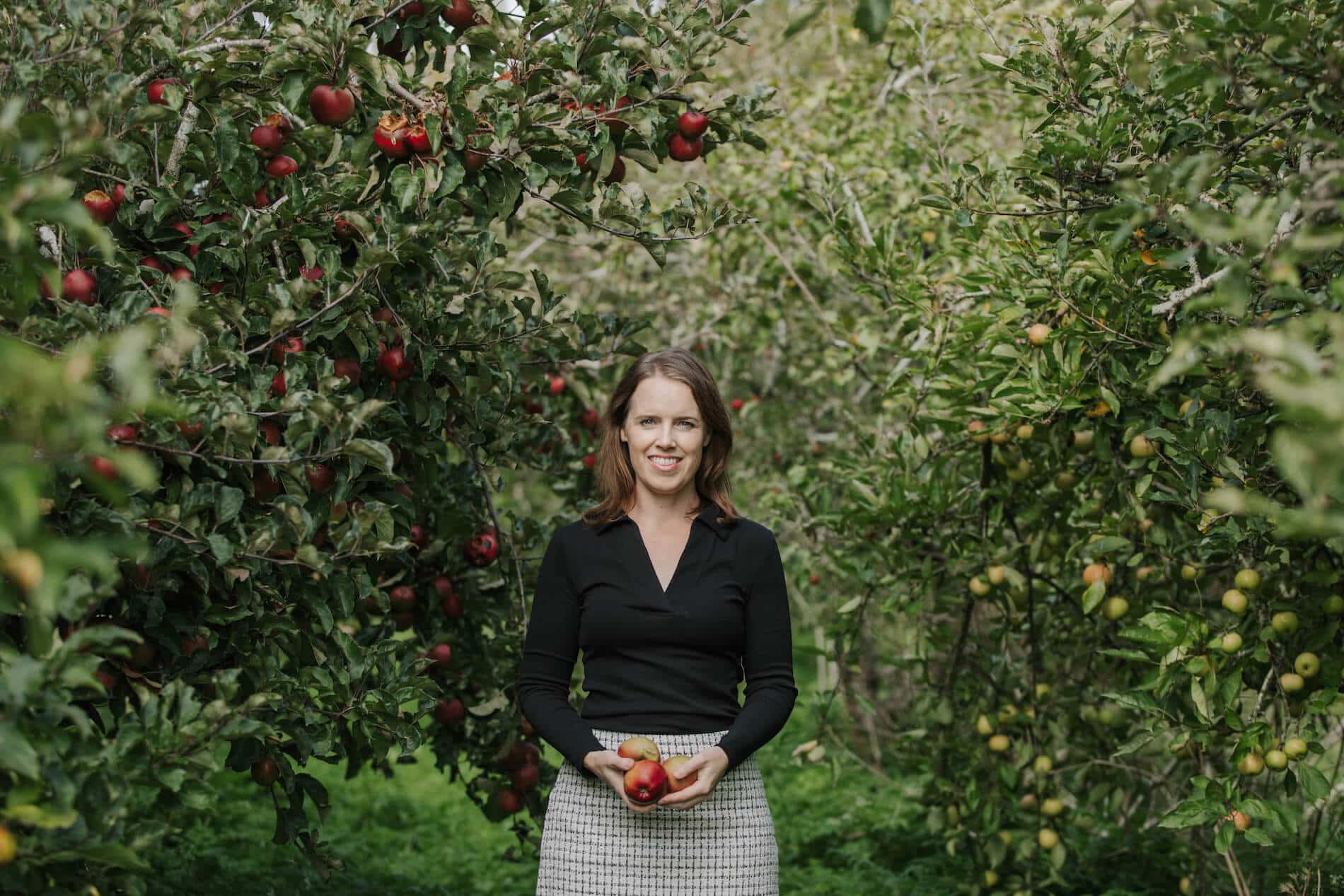 Dr Shannon Davis stands in an apple orchard, holding apples