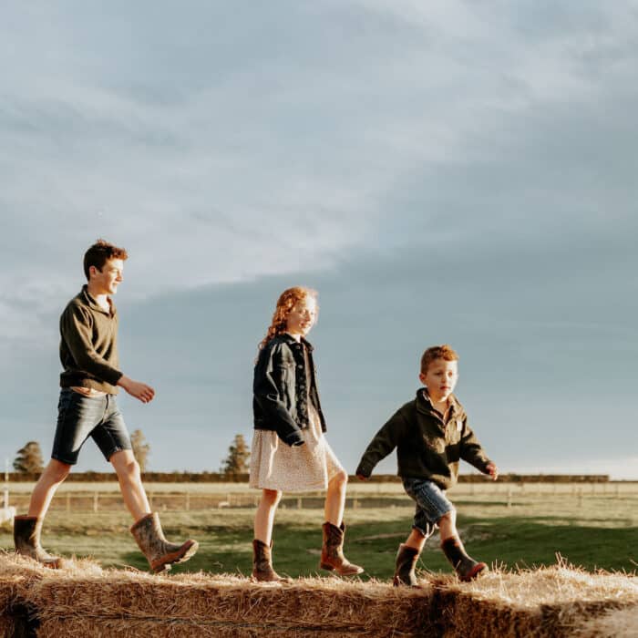 Three kids walk along hay bales on a farm.