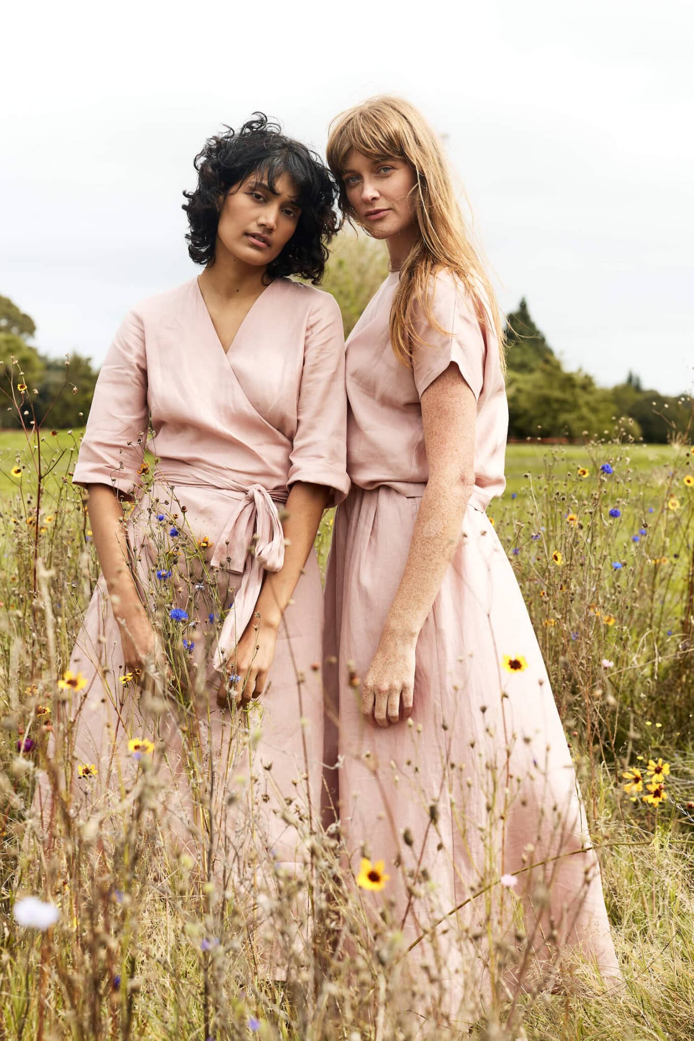 Two women standing in a field of wildflowers wearing matching pink dresses.