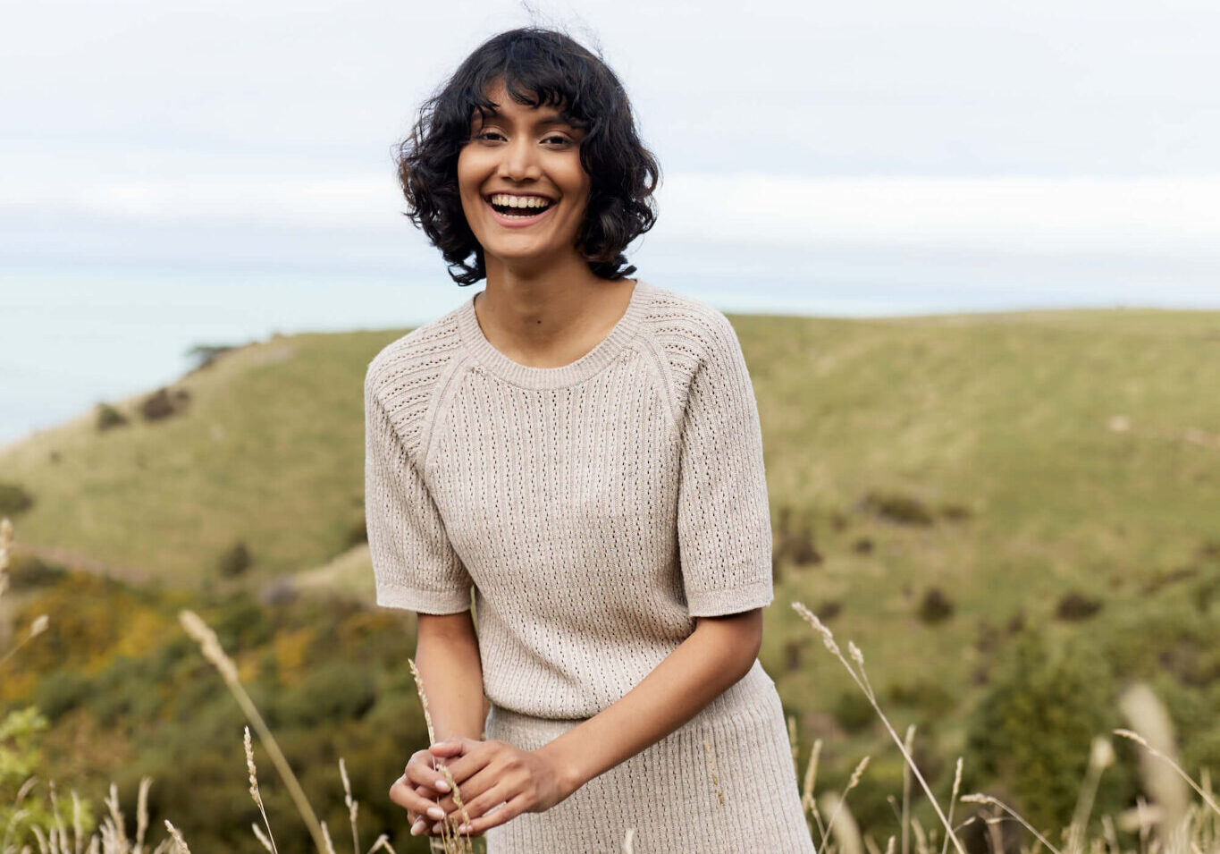 Woman in light brown clothing standing in a field of tall wild brown grass.
