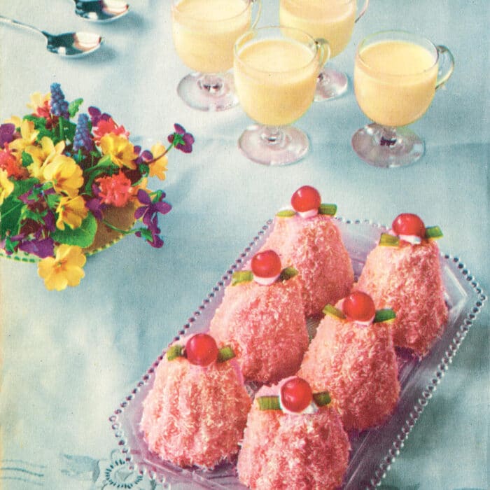 1950s photo of pink lamingtons and custard cups on a baby blue tablecloth.