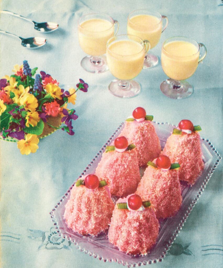 1950s photo of pink lamingtons and custard cups on a baby blue tablecloth.
