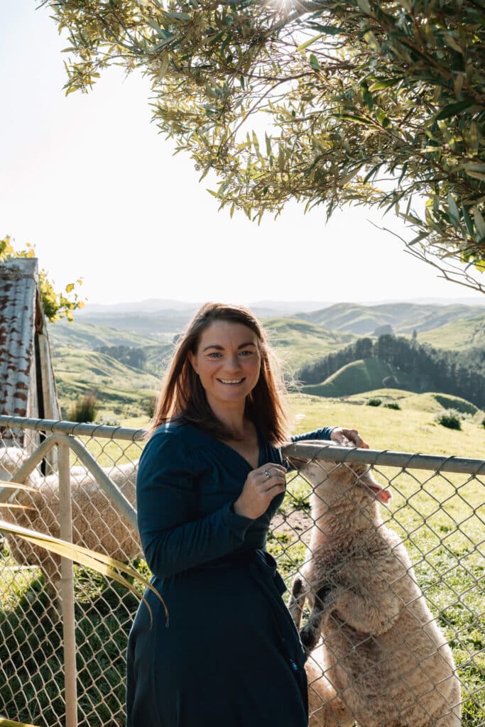 Woman leans against a farm gate and pats a sheep on the other side.