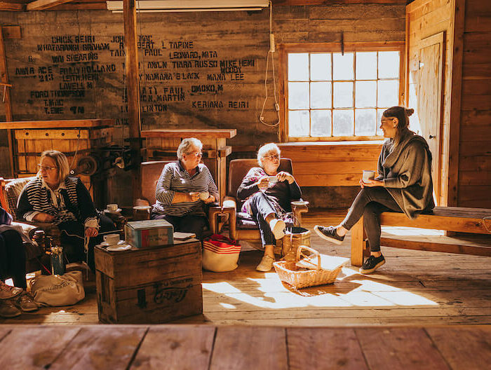 a group of women sitting, chatting and laughing, inside a woolshed